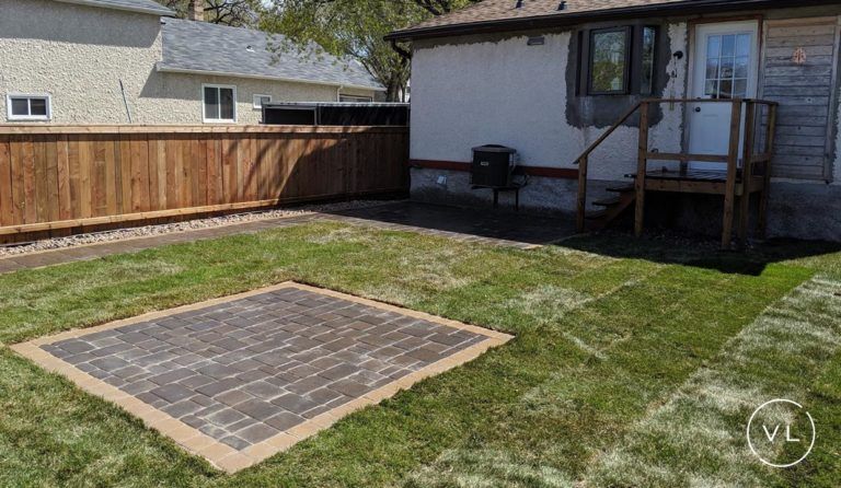 Backyard with brick patio, new grass, wooden fence, and house with back door.