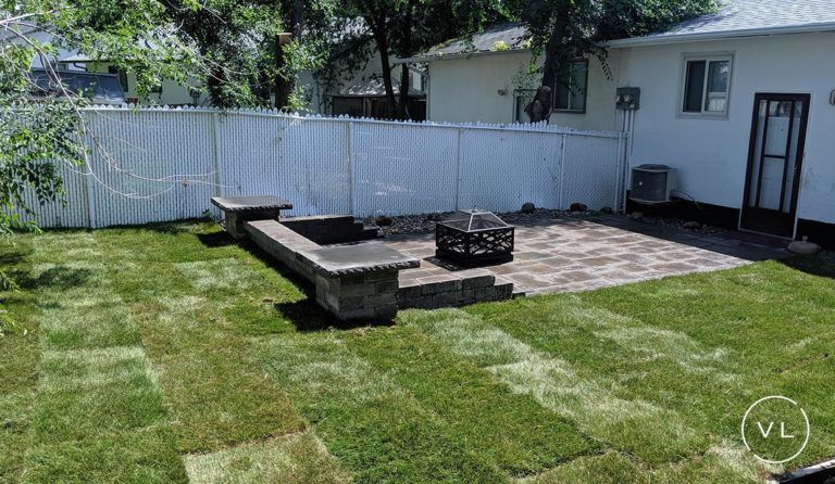 Backyard patio with fire pit, stone seating, and newly laid sod in a residential area.