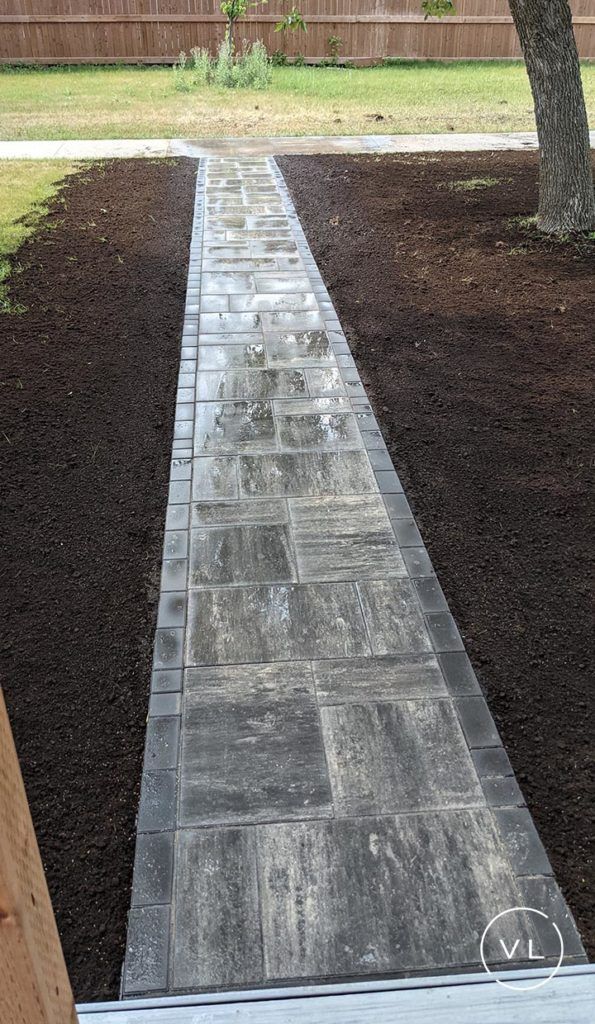 Stone pathway through dark mulch, leading to a lawn and wooden fence.