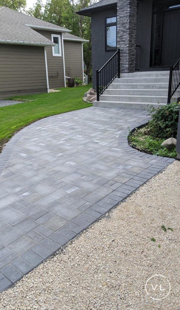 Gray brick pathway leading to a house with steps and a dark exterior; gravel border on one side.