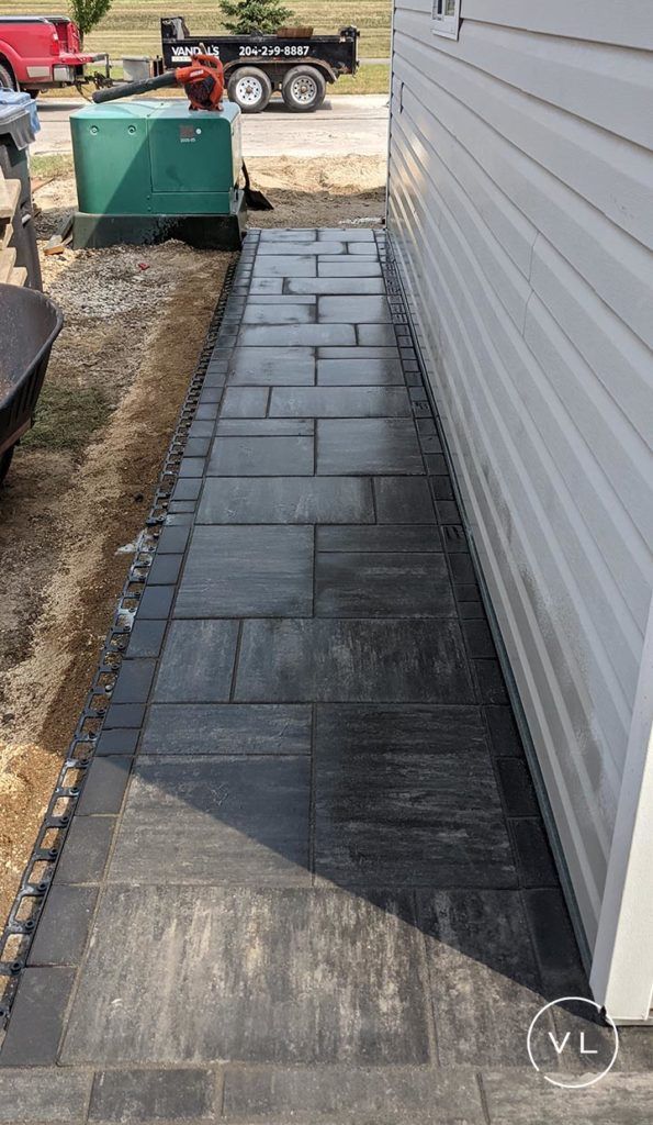 Dark stone pathway alongside a white house. Gravel border, and green generator visible.