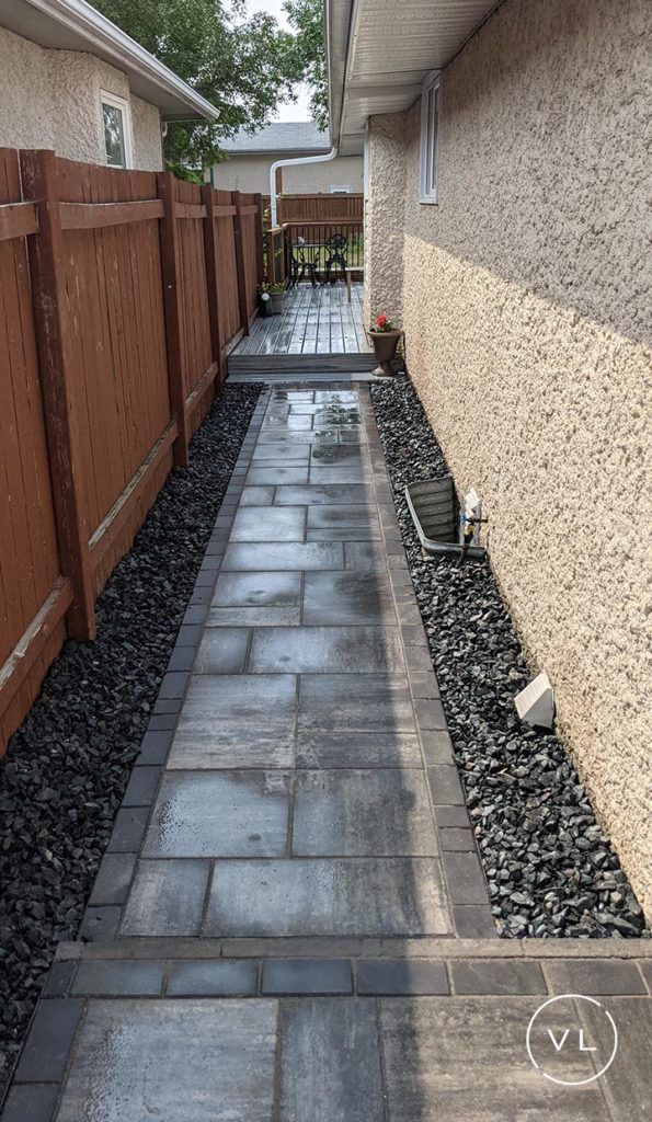 Narrow paved walkway between a brown fence and stucco wall, edged with black gravel.