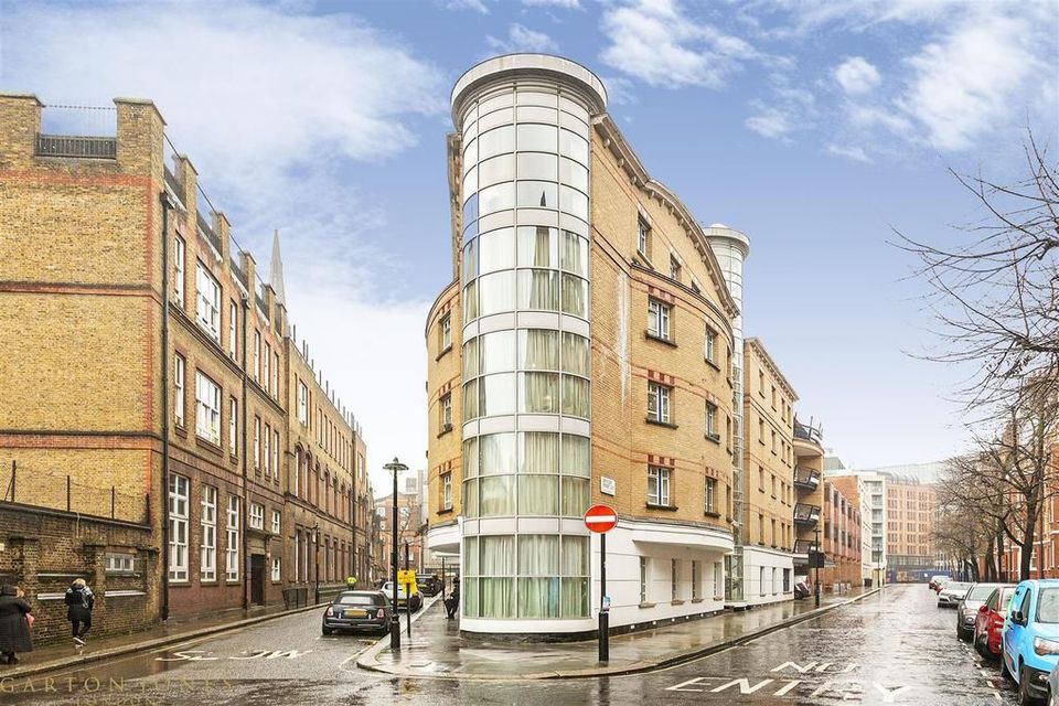 Street view of a curved corner building with a modern design, between older brick buildings on a rainy day.