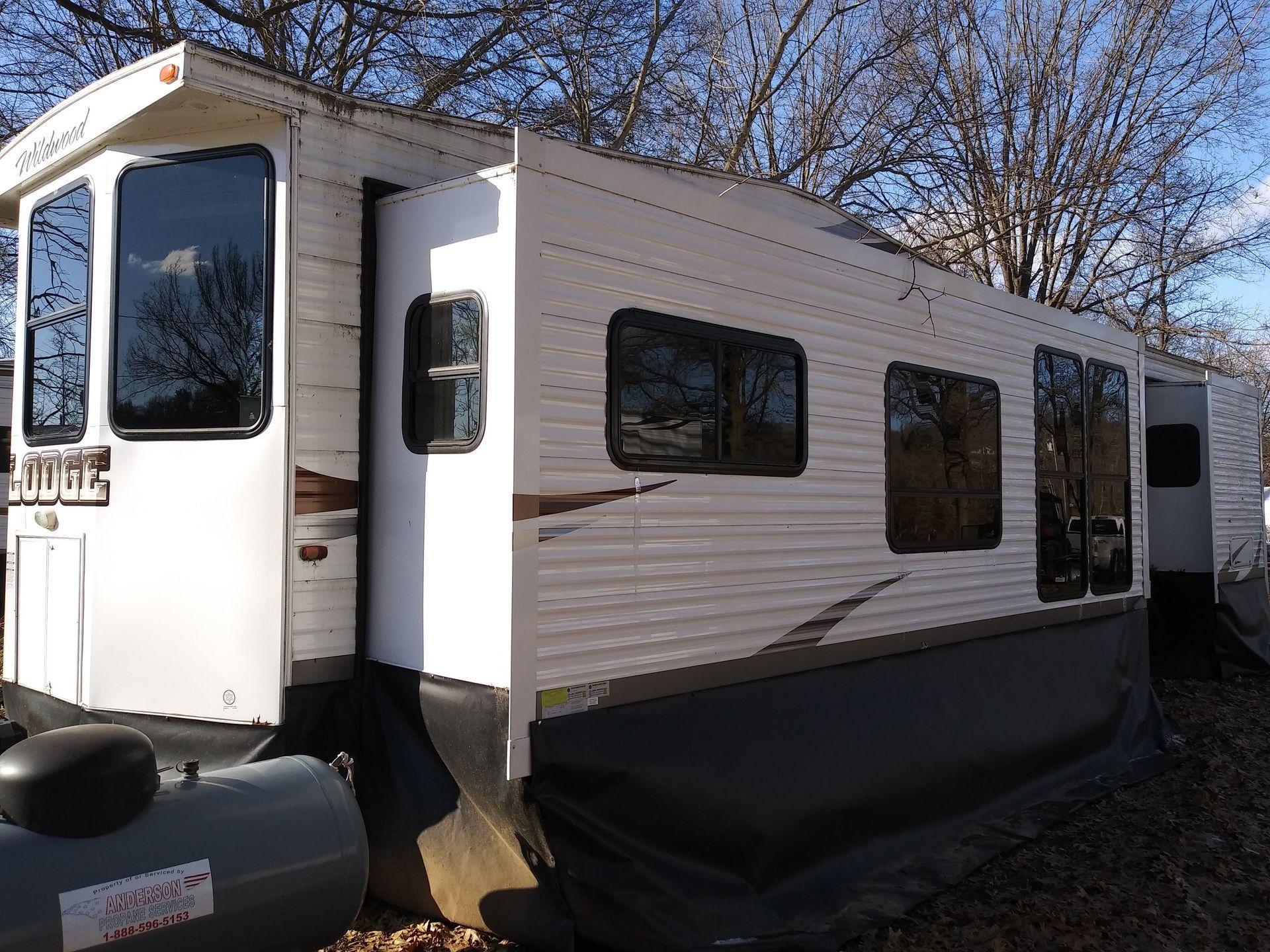 White travel trailer with black lower trim parked outdoors on a sunny day