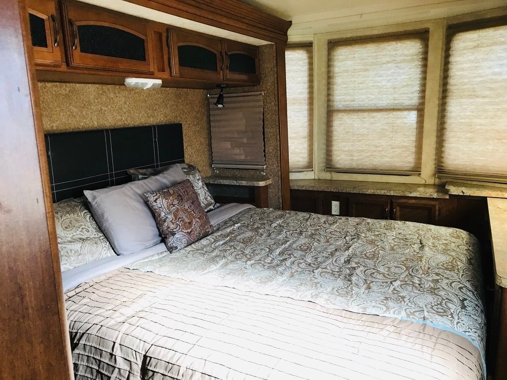Small bedroom with a made bed, wood-paneled cabinets, and windows with blinds