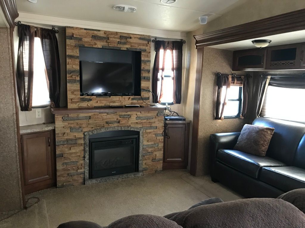 Cozy RV living room with stone fireplace, TV, windows, and a dark leather couch
