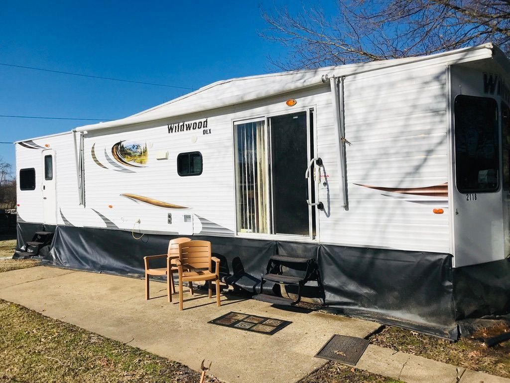 White RV trailer parked outdoors with a small table and chairs on a sunny day