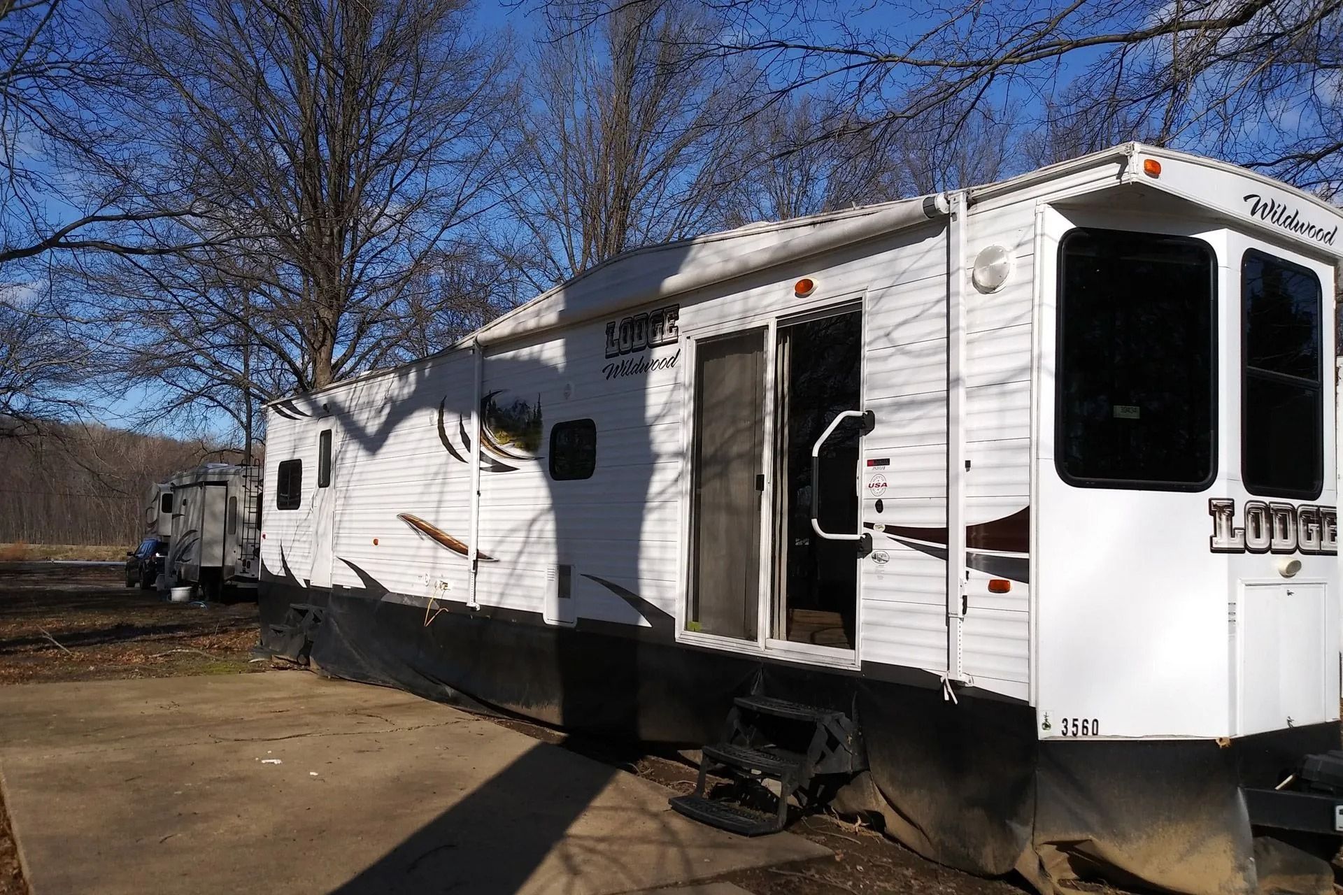 White RV trailer parked outdoors among bare trees on a sunny day