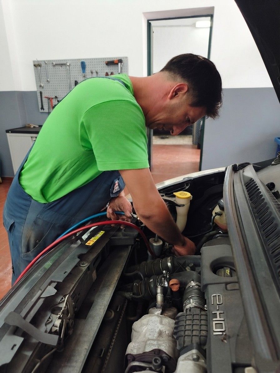 Meccanico con camicia verde al lavoro sotto il cofano di un'auto in un'officina.