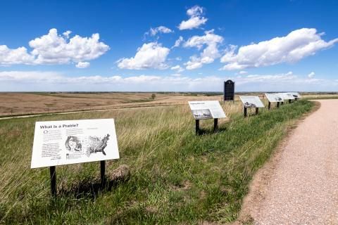 Interpretive signs along a grassy trail under a blue sky with clouds