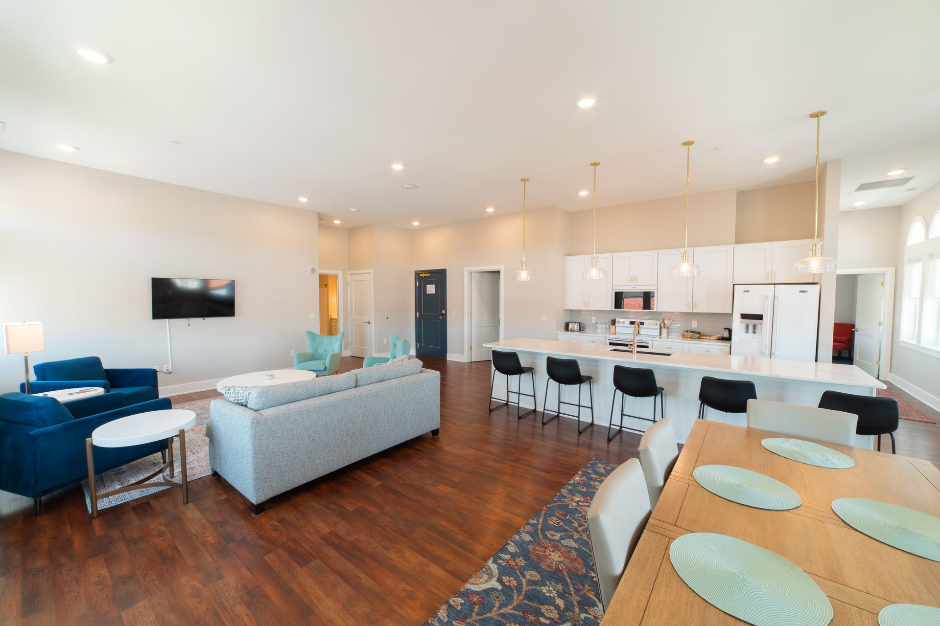 Bright open-plan living room with gray sofa, blue chairs, kitchen island, and dining table
