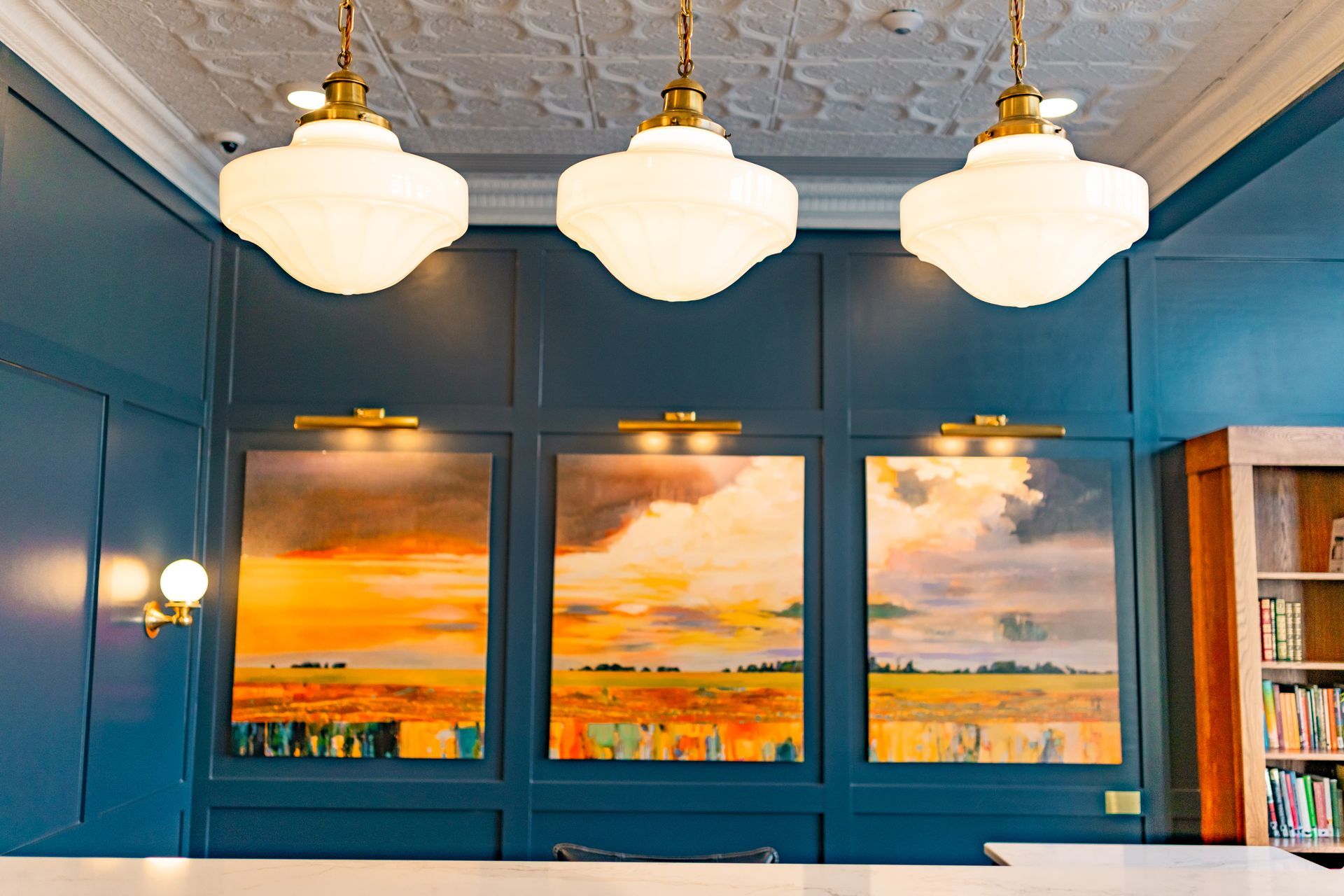 Blue paneled room with three framed sunset seascapes and hanging white pendant lights