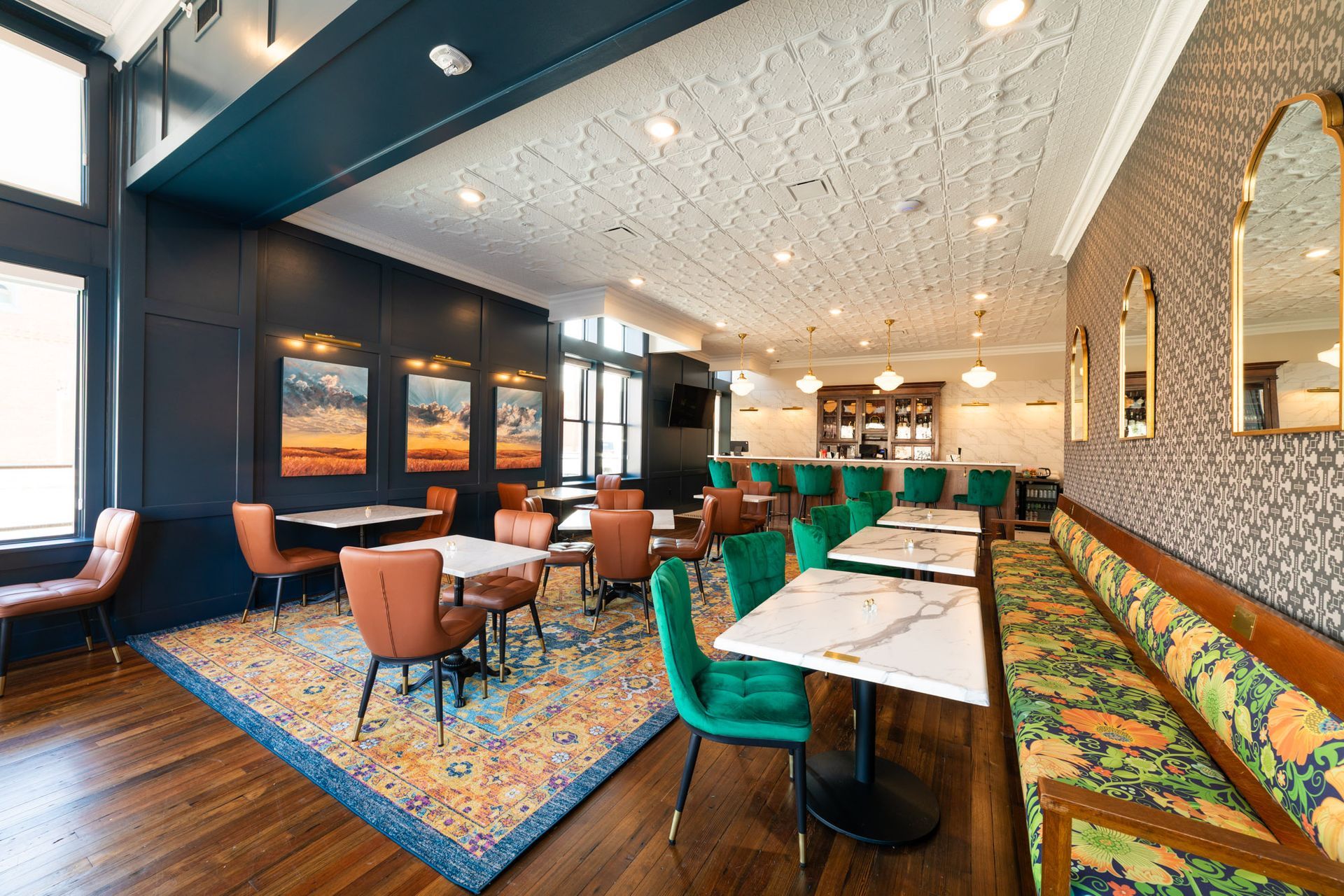 Restaurant interior with tables, chairs, bar, patterned carpet and wallpaper, and art.