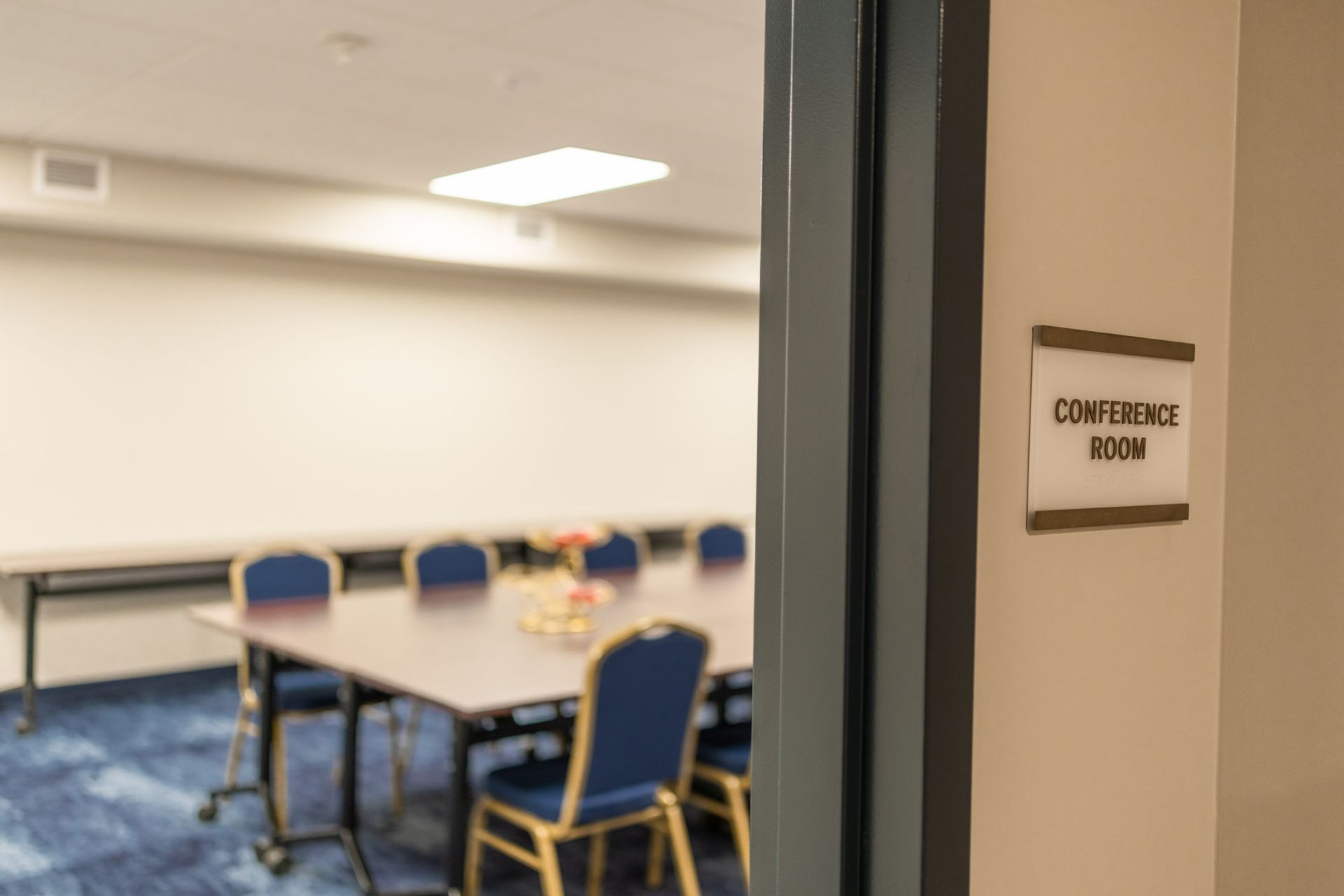 A view through a doorway into a conference room with a table, blue chairs, and a conference room sign on the wall.