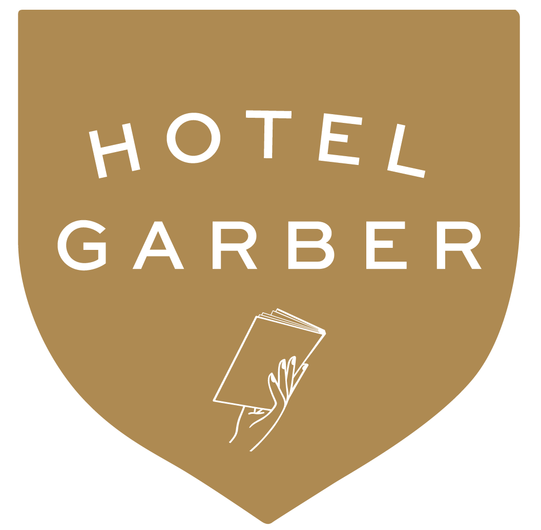 Hotel Garber logo in a gold shield; white text and hand holding papers.