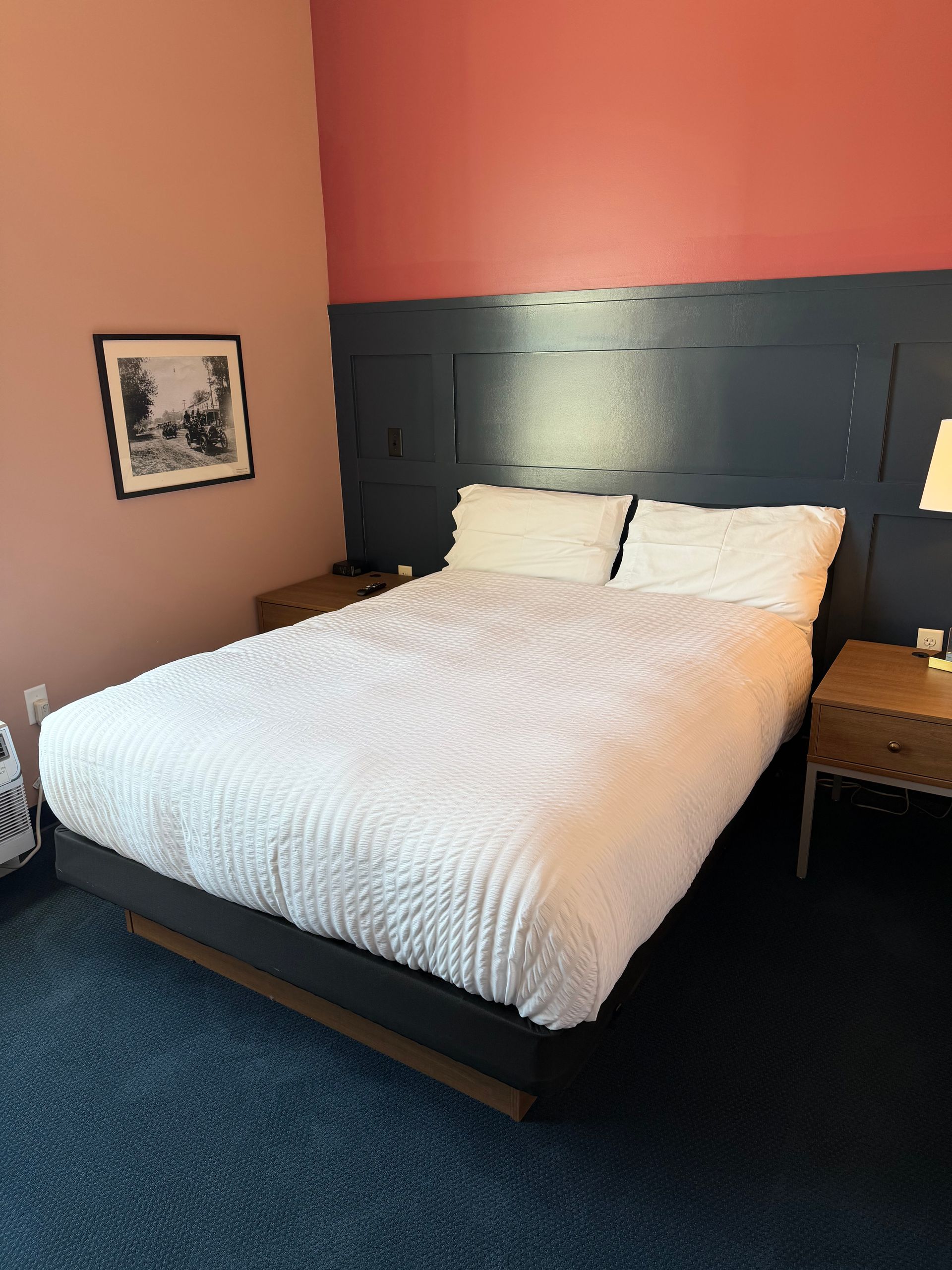 Bedroom with white bedspread, dark headboard, coral walls, and framed wall art