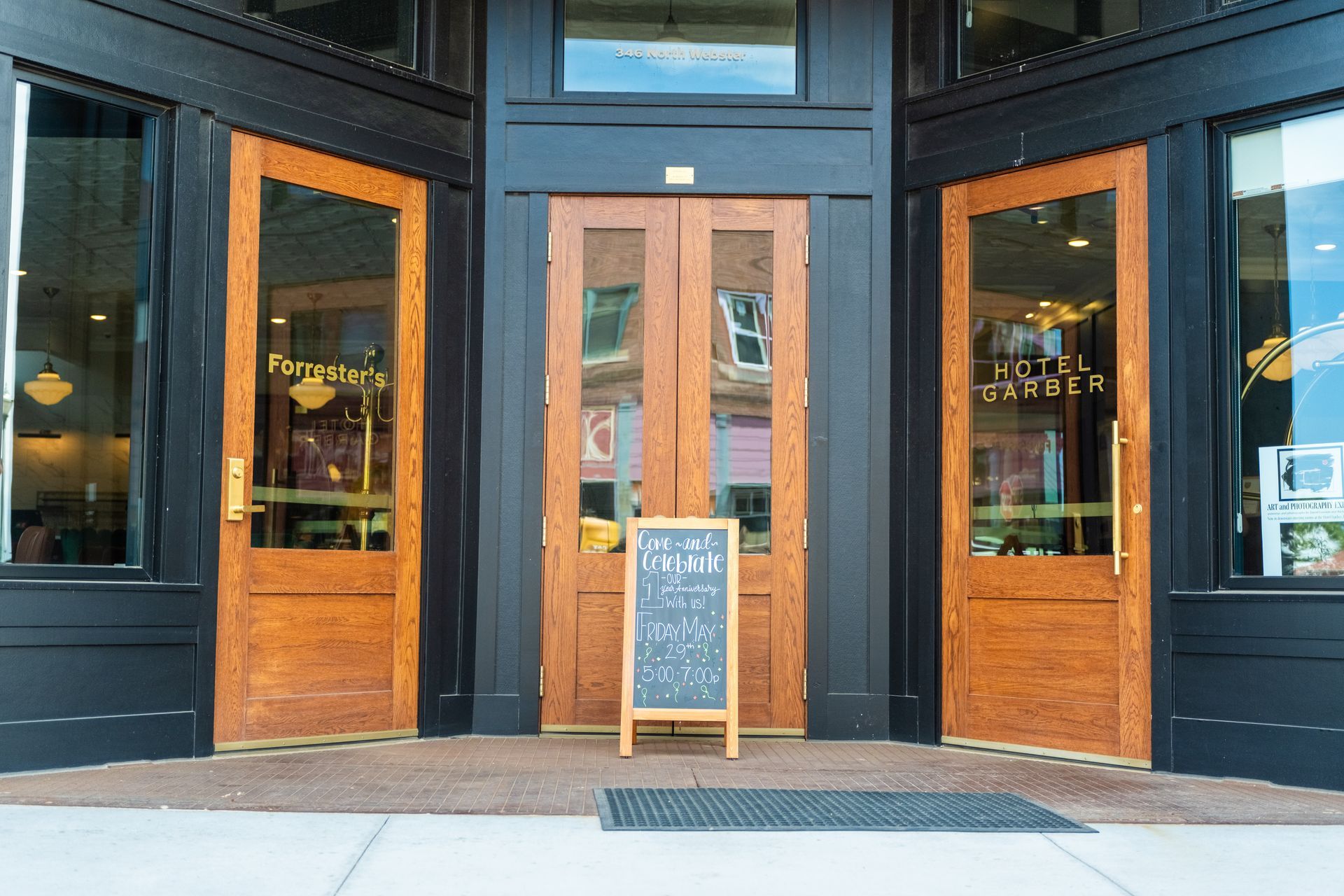Open storefront entrance with wooden double doors and a sidewalk chalkboard sign outside