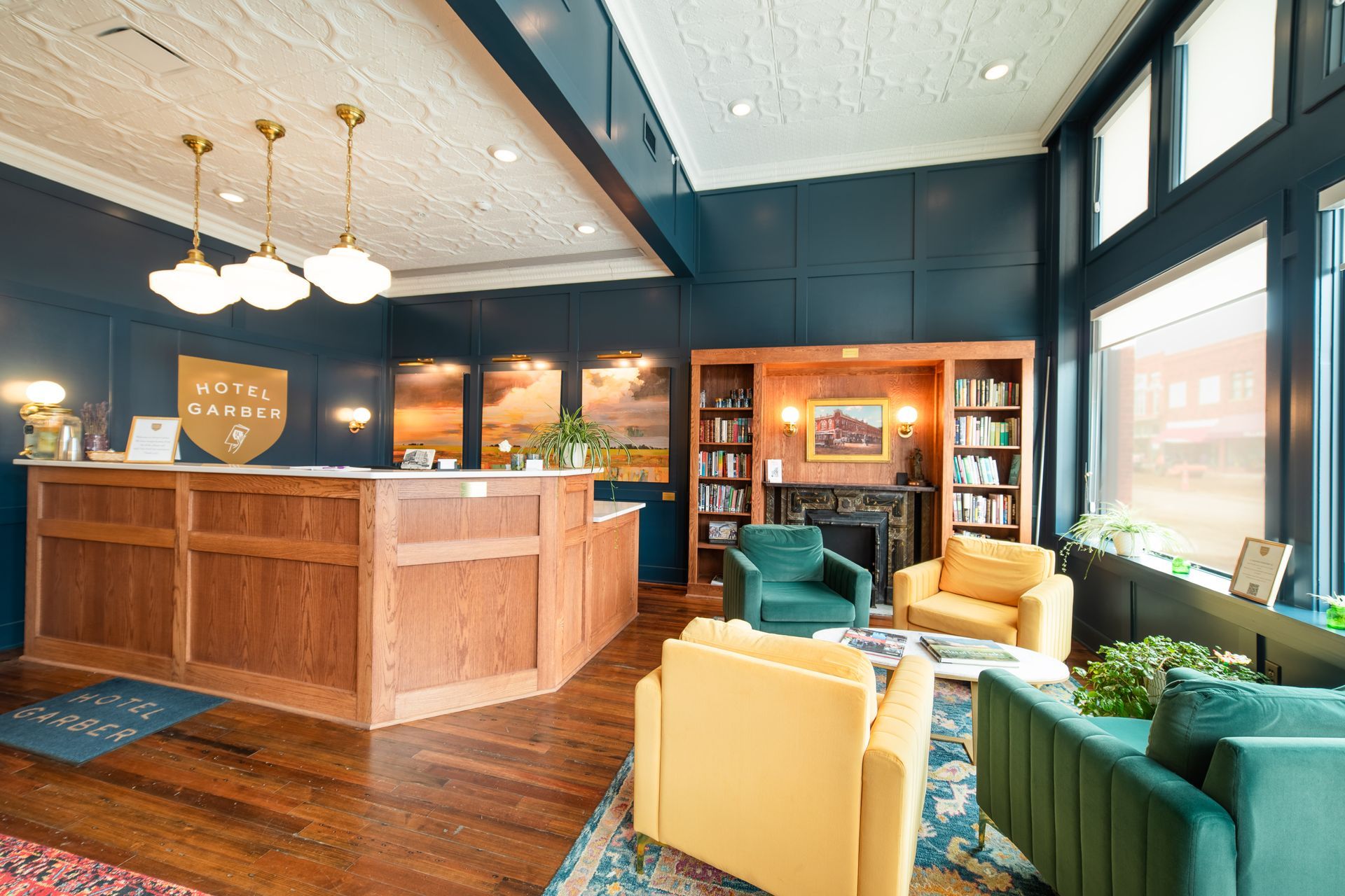Warm hotel lobby with wooden front desk, green and yellow chairs, and large windows.