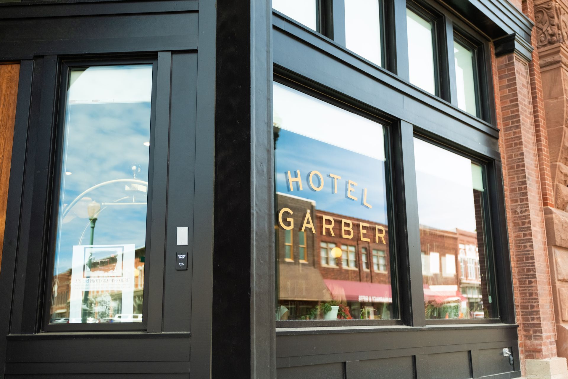 Storefront window reflecting a hotel sign on a brick street.