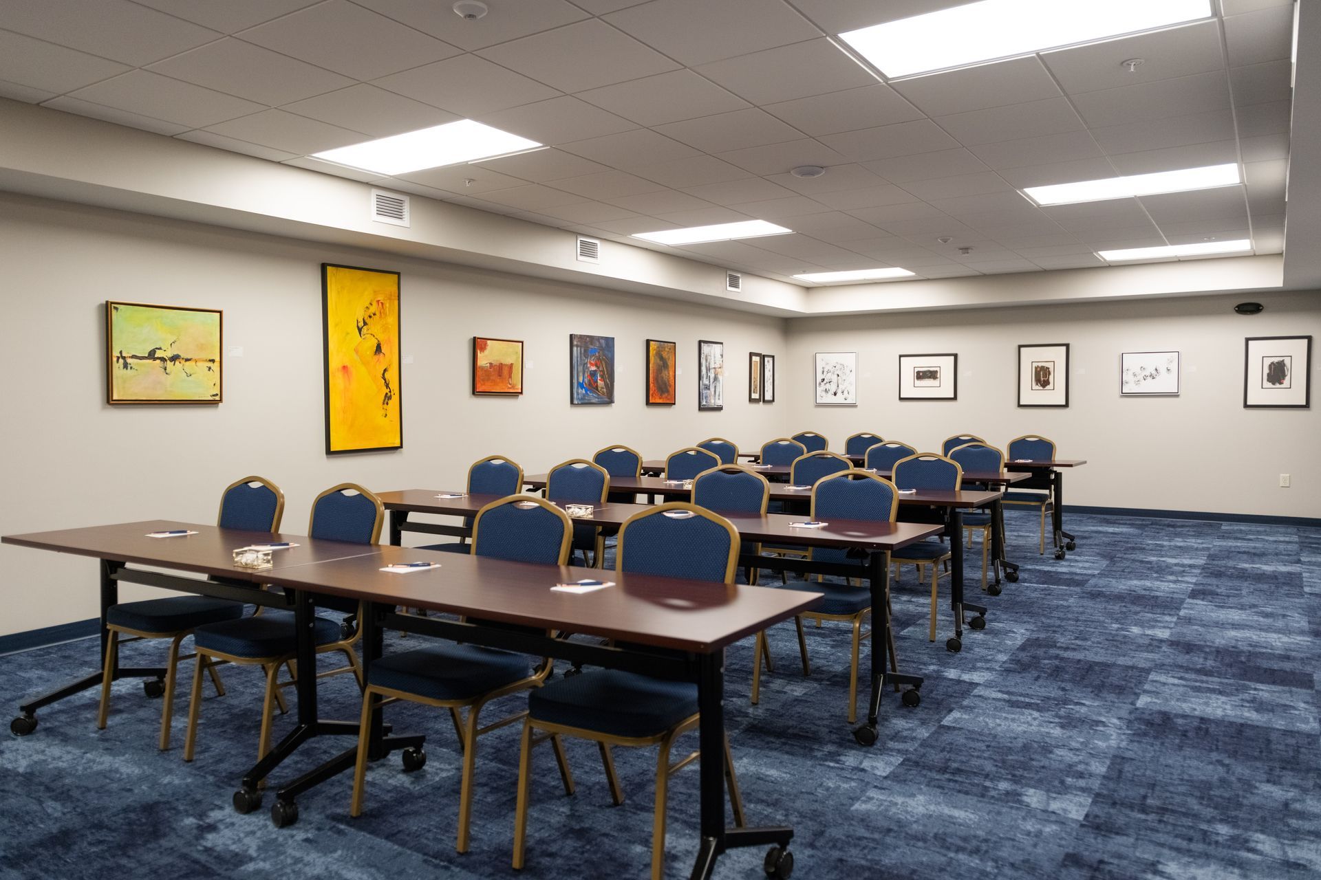 Empty conference room with rows of blue chairs, tables, and framed art on the wall