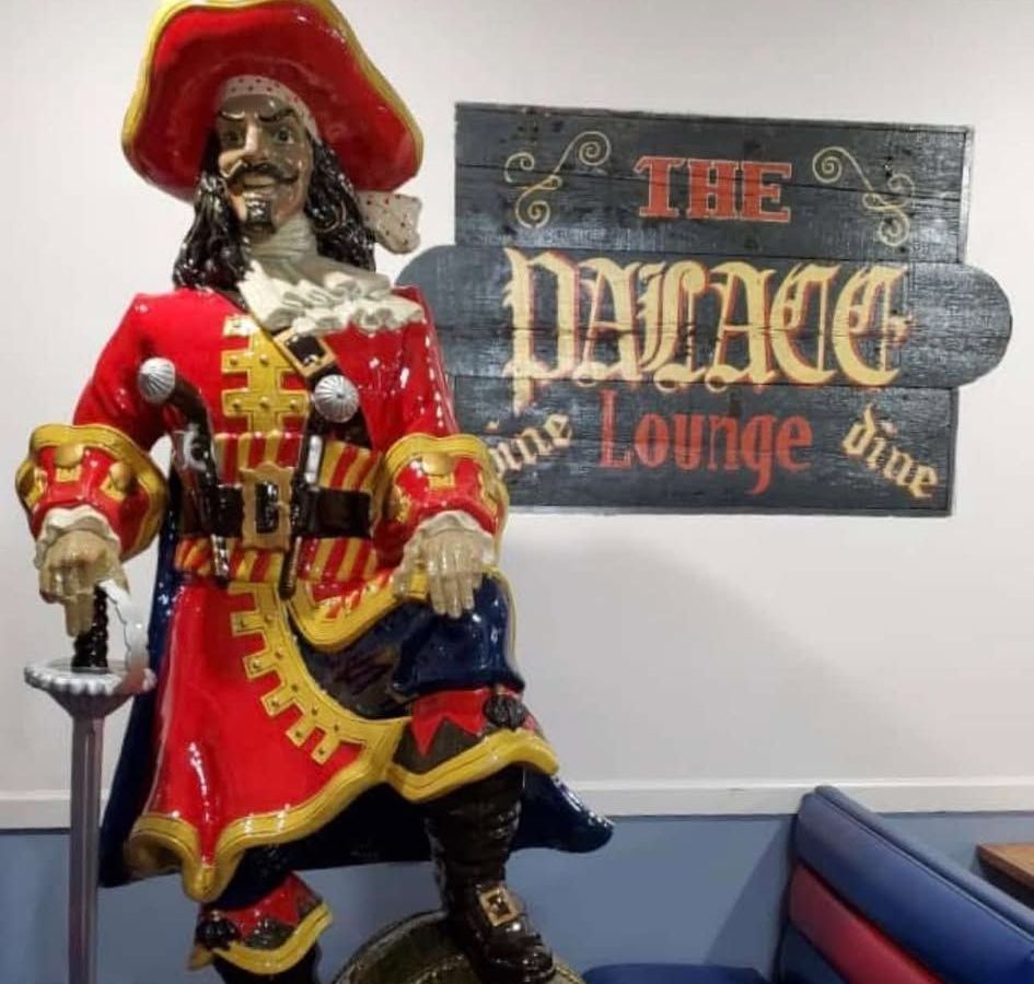 Statue of a pirate in red and gold attire stands next to a sign for 