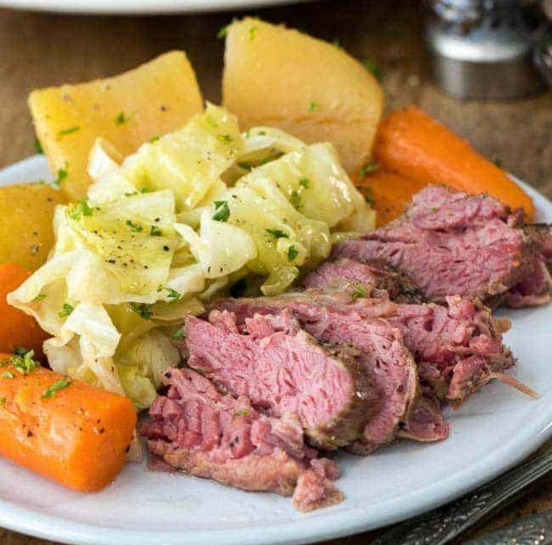 Corned beef and cabbage with carrots and potatoes on a white plate.