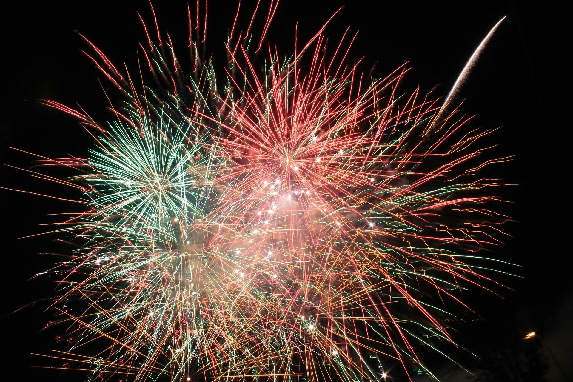 Fireworks in green and red burst against a dark night sky.