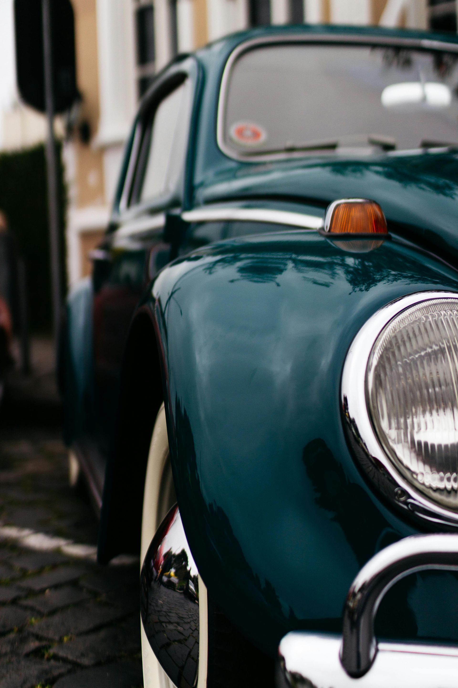 Teal vintage Volkswagen Beetle car with white tires, parked on a cobblestone street.