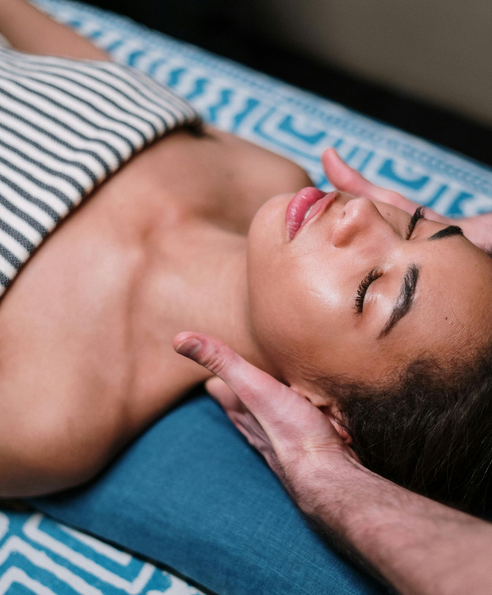 Woman receiving a head massage, eyes closed, on a massage table, hands supporting her head.