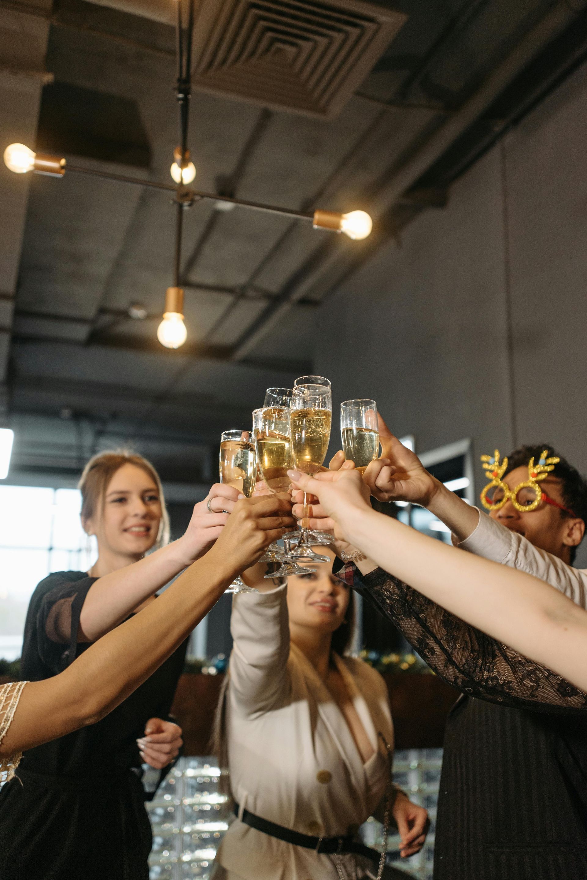 People toasting champagne flutes. They are indoors under pendant lighting.