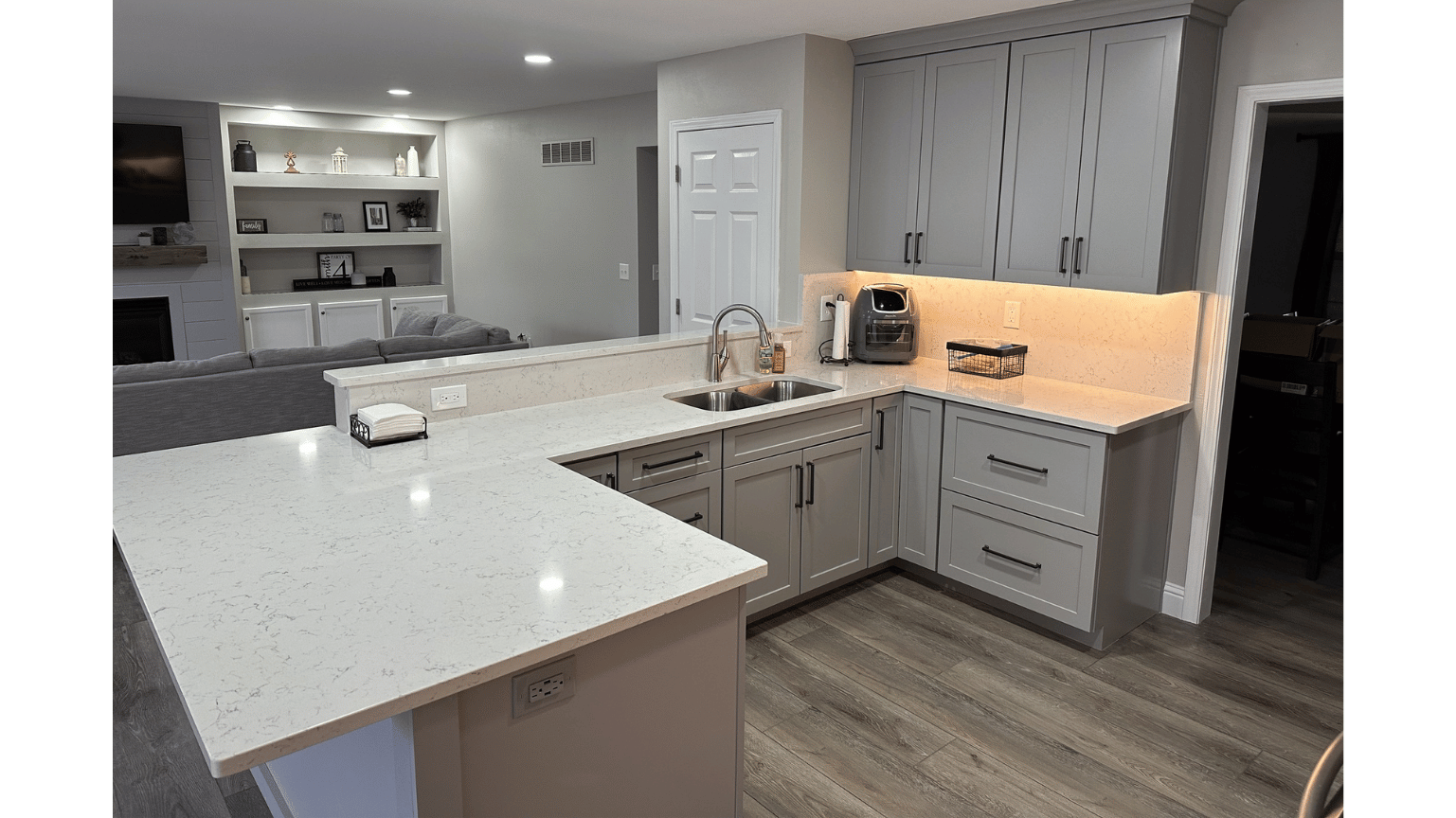 Modern kitchen with white countertops, gray cabinets, and a lit coffee nook near a window.