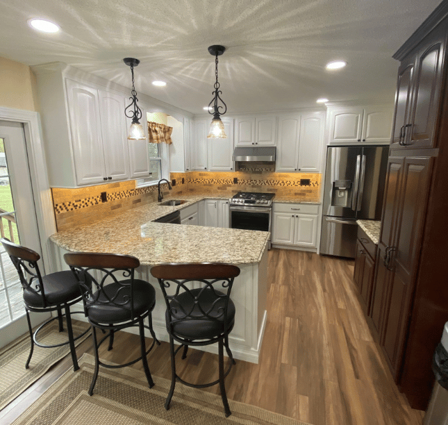 Modern white kitchen with granite island, black barstools, pendant lights, and stainless steel appliances