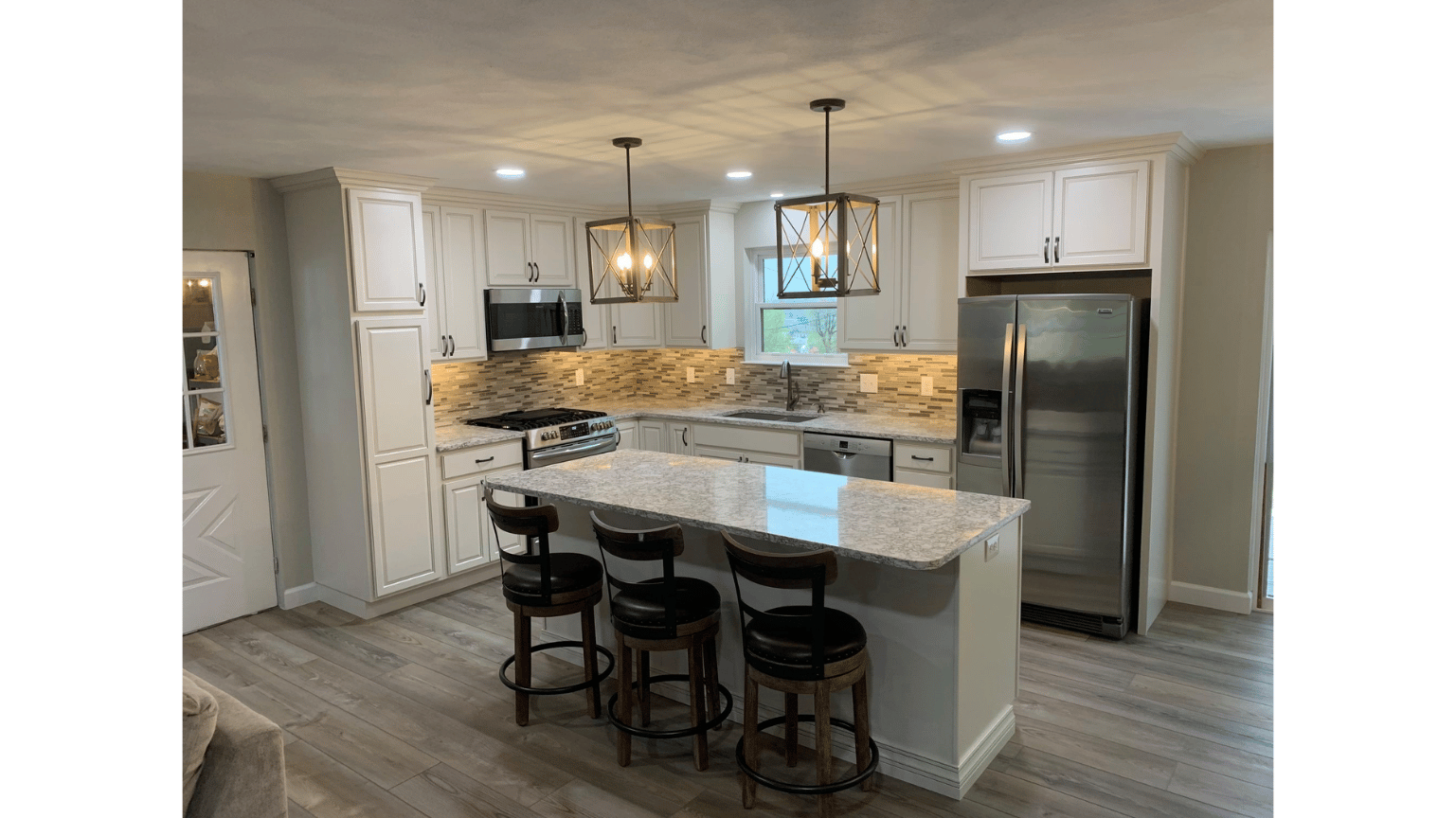 Modern white kitchen with island, black bar stools, pendant lights, and stainless steel refrigerator