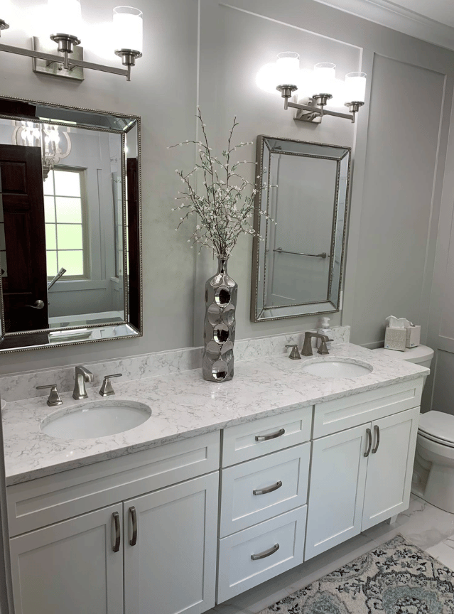 Bright bathroom with white vanity, marble countertop, two mirrors, and silver wall sconces