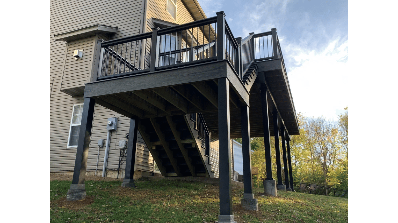 Raised wooden deck on a stone house, viewed from below, with stairs and autumn trees in the background