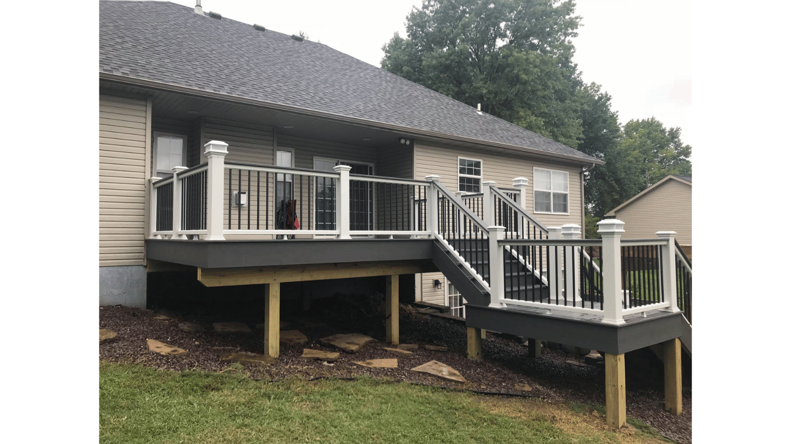 Raised house deck with white railings and stairs on stilts in a wooded yard