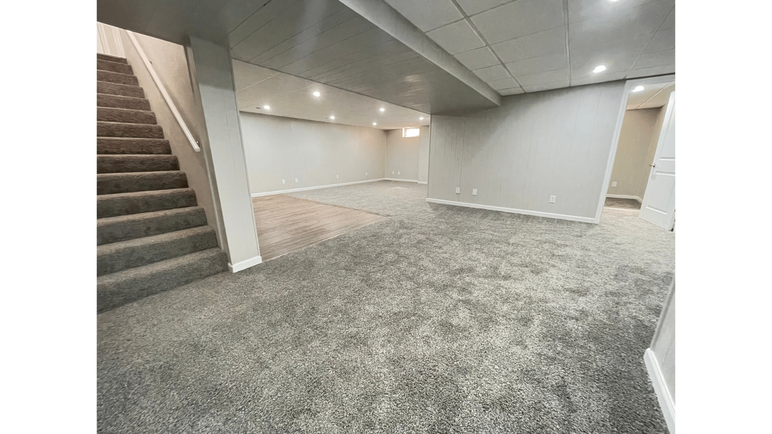 Empty finished basement with carpet, stairs, recessed lights, and white walls.