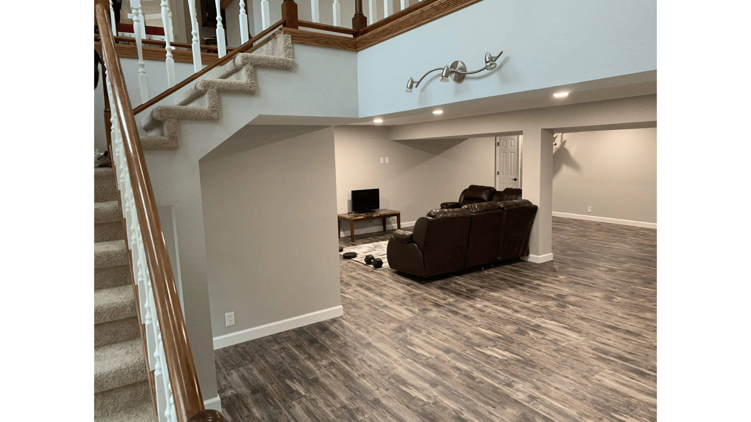 Modern finished basement with gray walls, wood-look floor, staircase, and a brown sectional seating area