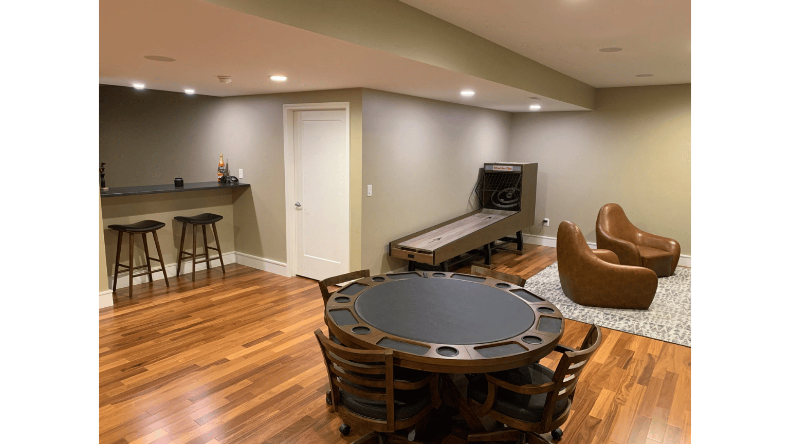 Basement rec room with bar stools, poker table, TV, and leather chairs on wood and carpet flooring
