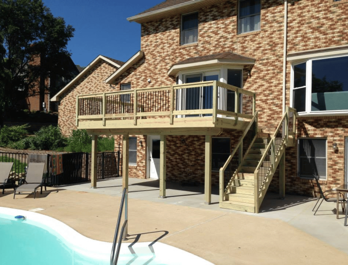 Backyard patio with a wooden deck overlooking a swimming pool beside a brick house.