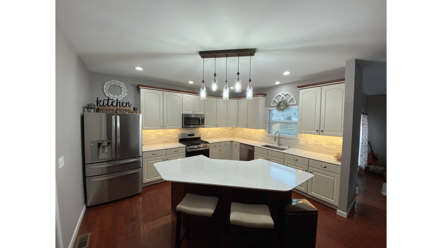 Modern kitchen with stainless fridge, white cabinets, island, pendant lights, and dark wood floors