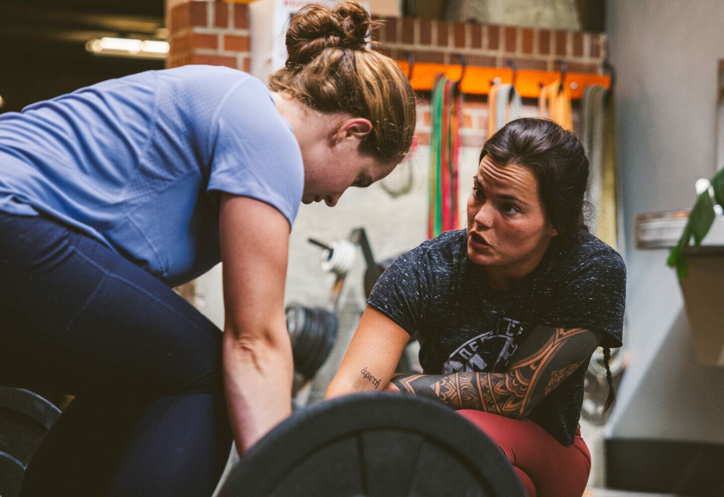 Two women at Derby City Fitness in Louisville, KY; one spotter coaching the other who's lifting a barbell.