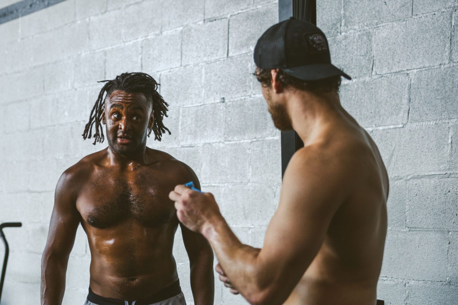 Two sweaty men in a Louisville gym; one has dreadlocks and is being assisted by another wearing a hat.