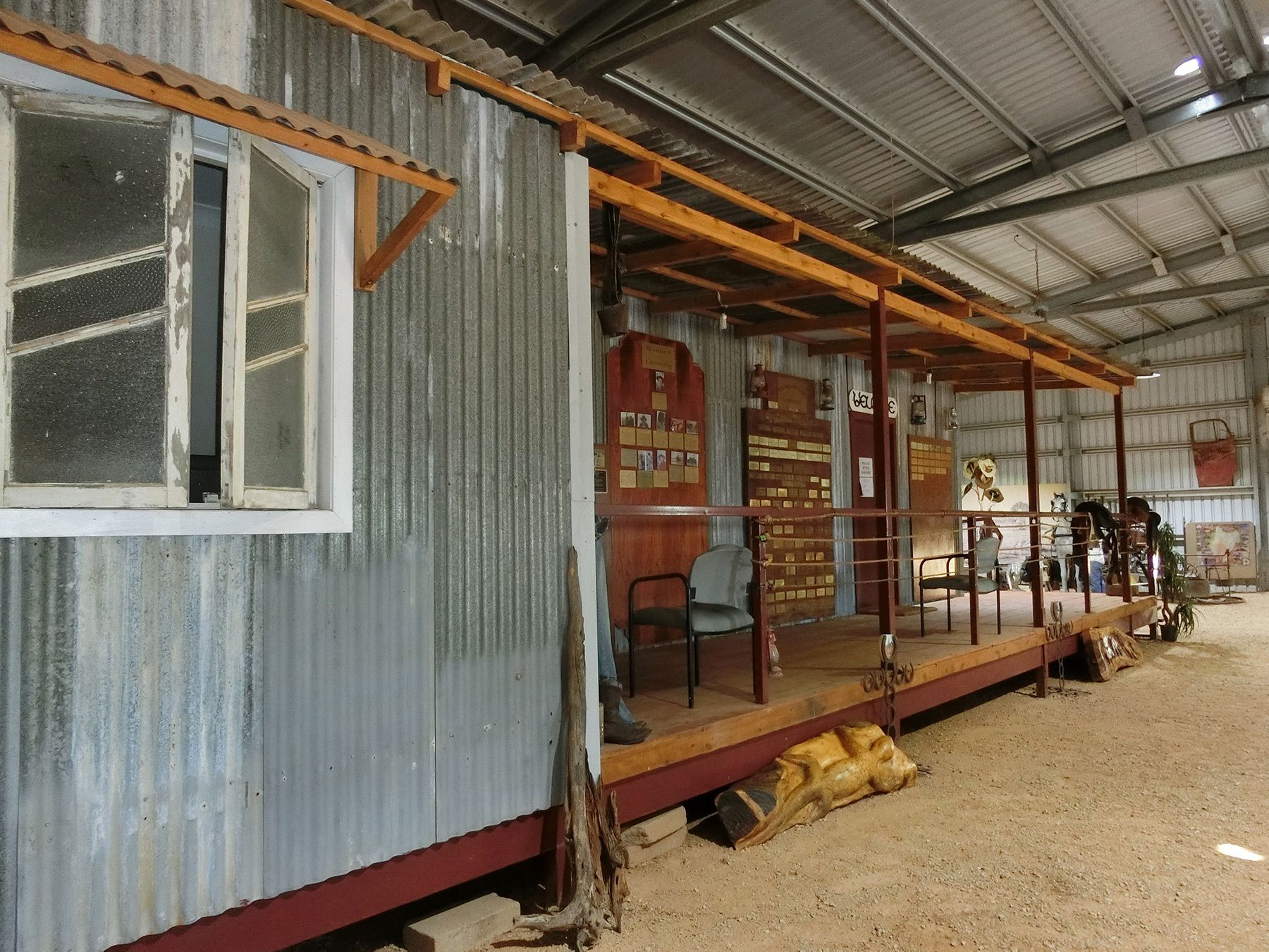 Corrugated metal building with a porch under a roofed shelter, outdoors on gravel.