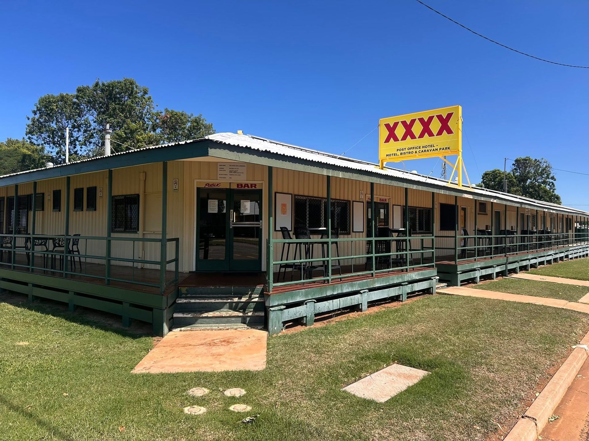Motel-style building with wraparound porch and a large yellow XXXX sign on a sunny day