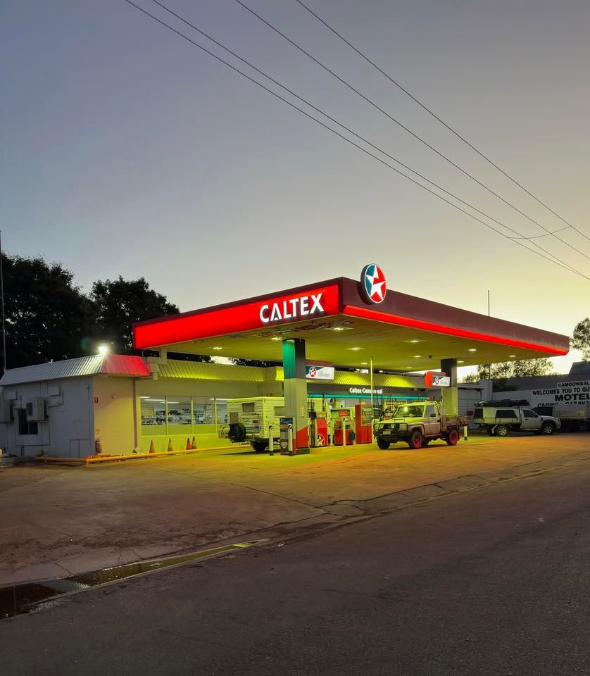 Caltx gas station at dusk with red-lit canopy and parked vehicles