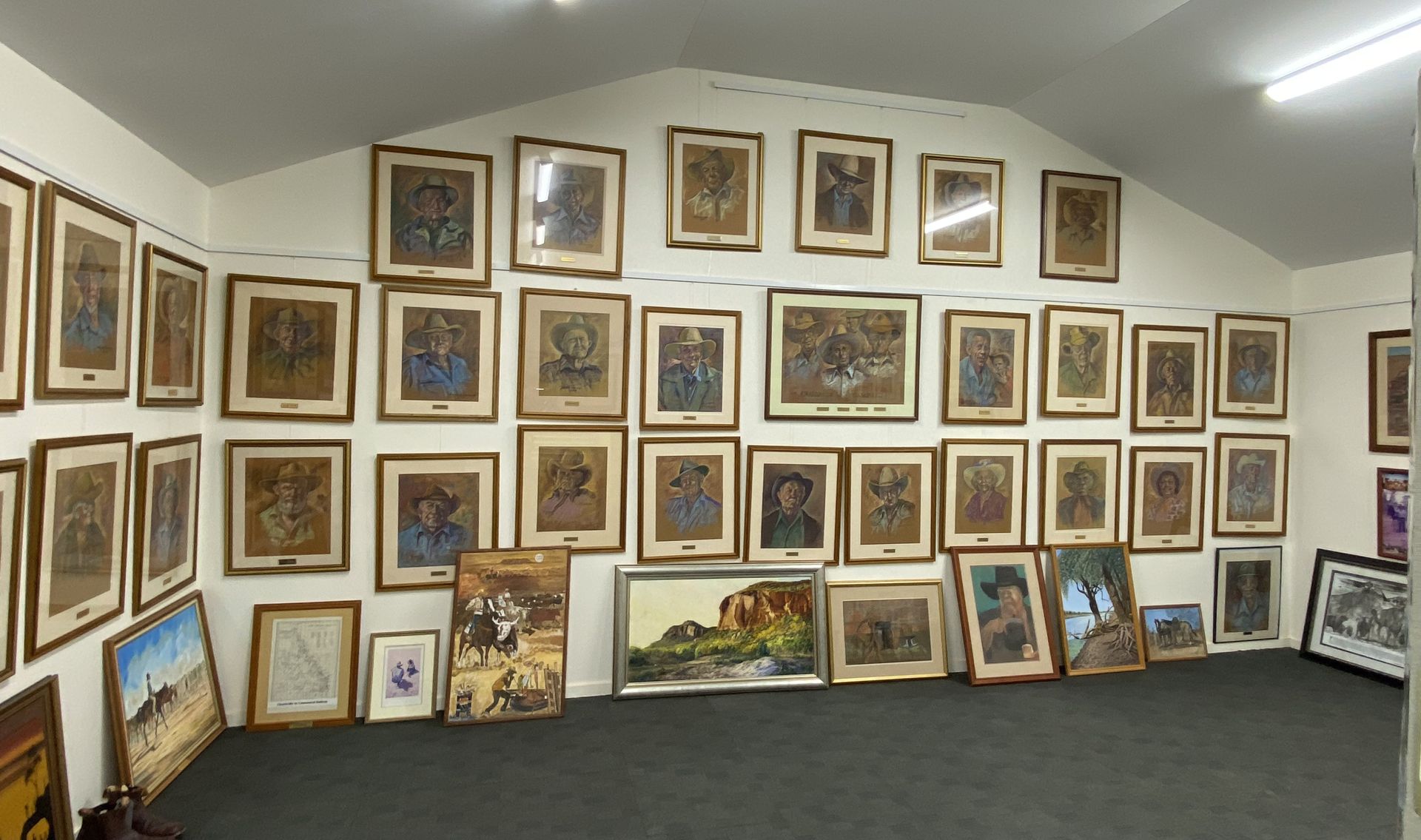 Gallery wall with many framed paintings and drawings arranged on a white wall and floor along the room