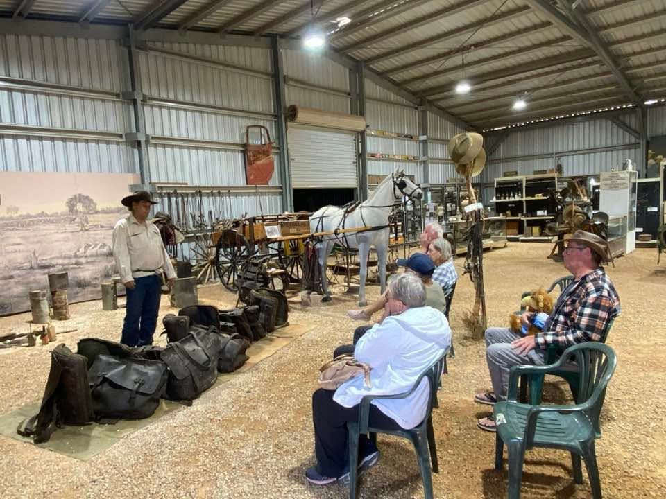 Instructor speaking to seated audience in a barn workshop with tools, equipment, and straw on the floor