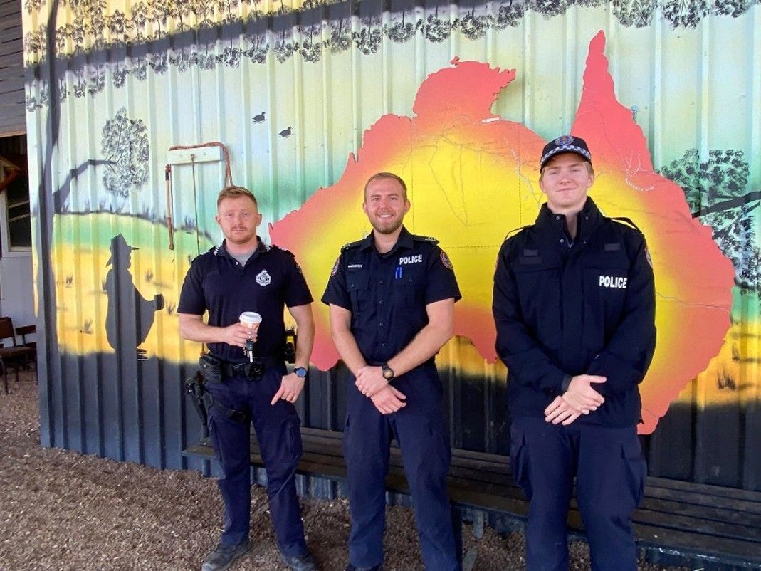 Three uniformed officers standing in front of a colorful mural outdoors