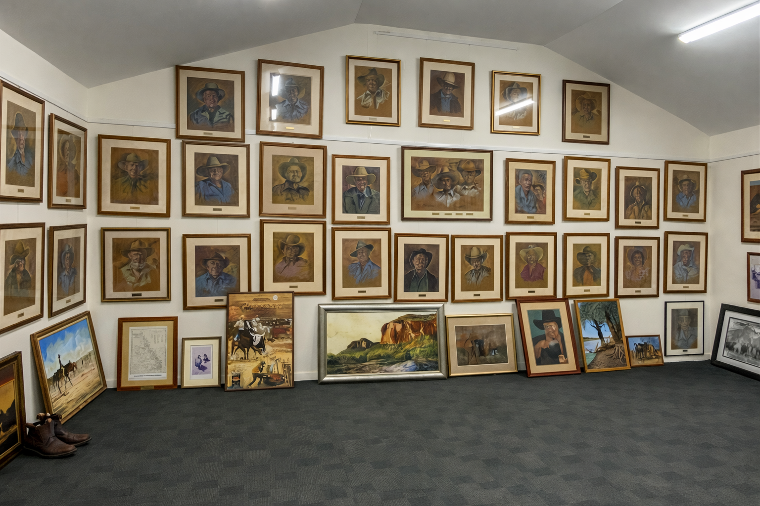 Art gallery room with dozens of framed paintings covering two walls and leaning along the floor.